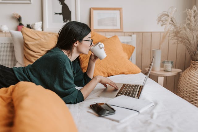 Woman using laptop and drinking beverage in bed
