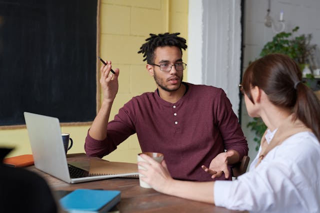 Man and woman sat at an office desk and talking.