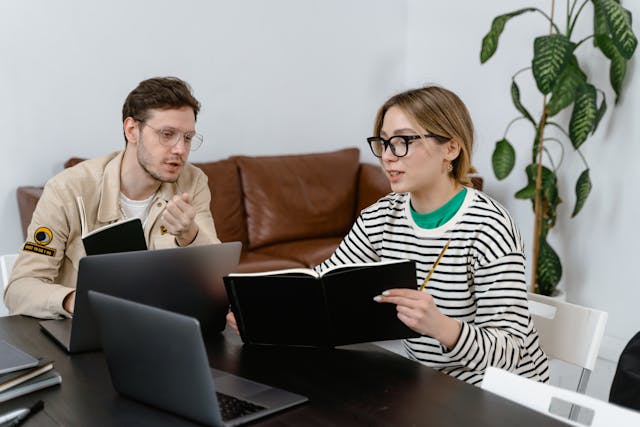 Woman showing notebook to a man sitting next to her to learn a foreign language with him.